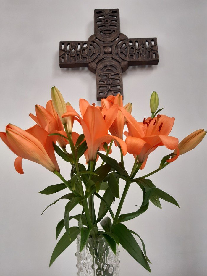 Orangefarbener Lilienstrauß vor Kreuz
